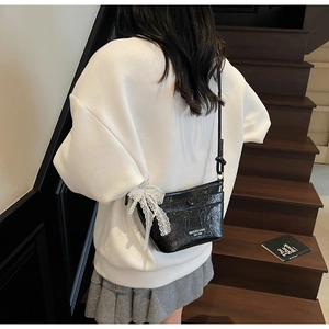Detail of black glossy crossbody bag with white lace bow and elegant pearl chain