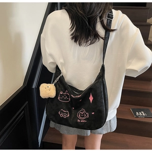 Detailed view of black crescent bag with cat embroidery and plush pendant on strap