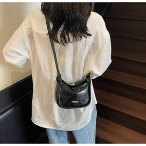 Detail of a black wrinkled patent leather crossbody bag with silver buckle and logo
