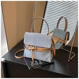 Detailed texture of blue denim handbag with brown leather straps and gold buckle trim