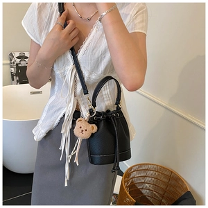 Detail of black leather bucket bag with white stitching and cute bear charm