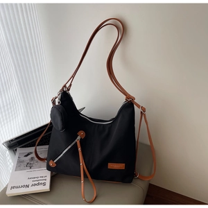 Close-up of black nylon tote bag with brown leather strap and side zipper detail