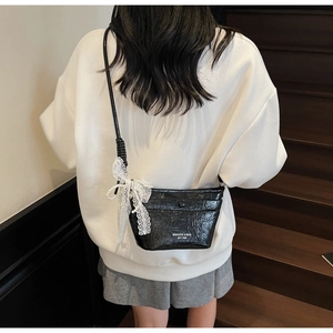 Detail of black glossy crossbody bag featuring white lace bow and pearl decoration