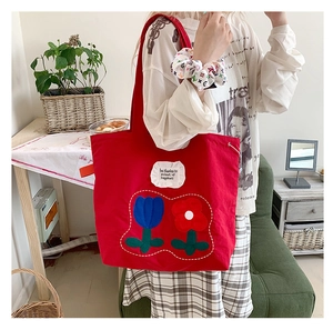 Detailed close-up of a red canvas tote bag featuring floral tulip embroidery and fabric tag