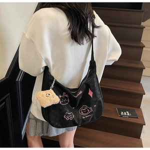 Detail of black hobo bag with pink cat embroidery and plush charm on wooden stairs
