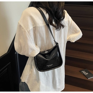 Detail of a black patent leather crossbody bag with silver twist lock on a shoulder strap