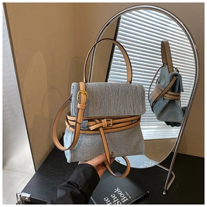 Detail of blue denim handbag with brown leather trim, gold buckles and crossbody strap