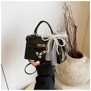 Detail of black crocodile texture mini bag featuring white lace bow and pearl chain