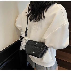 Detail of black pleated crossbody bag featuring a lace bow and faux pearl charm accessory