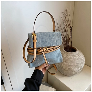 Detail view of light blue denim handbag with brown leather straps and gold buckle