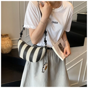 Detail of black and white striped woven straw bag with adjustable knotted strap and floral charm