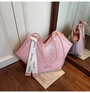 Detail of pink pleated tote bag with decorative silk scarf and metallic logo emblem