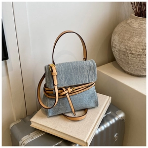 Detail of blue denim tote bag with brown leather trim and golden hardware on a white book