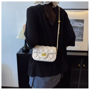 Detailed view of white quilted crossbody bag with gold chain strap on a person