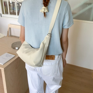 Detail view of a cream leather crescent bag with adjustable wide shoulder strap on model