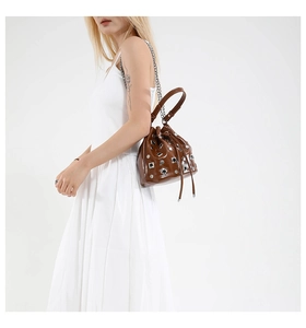 Brown rivet bucket bag with hollow details and chain strap shown on model in white dress