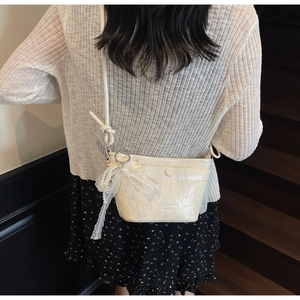 Detailed close-up of cream crossbody bag with pearl strap and lace bow charm detail