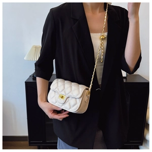 Close-up of beige quilted crossbody bag with gold ball chain strap on a stylish model