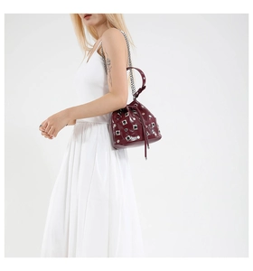 Detail of wine red patent leather bucket bag with silver studs and chain strap on model
