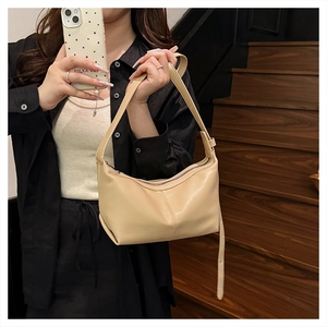Close-up of beige half-moon shoulder bag with zipper closure on model in a staircase setting