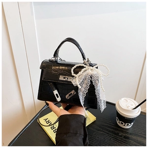 Detail of black crocodile texture handbag with pearl bow and silver clasp closure