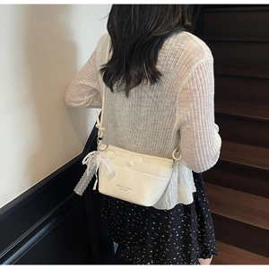 Detail of cream crossbody bag with pearl lace bow charm worn by a model in black floral dress