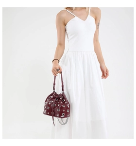 Detail of burgundy bucket bag with silver studs and drawstring closure held by a model