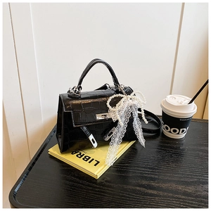 Detail of black crocodile-pattern handbag with silver clasp and pearl bow charm