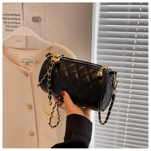 Détail d'un sac cylindrique noir matelassé avec chaîne dorée et coutures de luxe