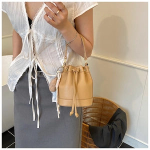 Detail of light brown bucket bag with drawstring closure and stylish fur pompom charm