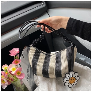 Detail of striped straw woven dumpling bag featuring a sunflower pendant and black strap