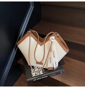 Detail of off-white tote bag featuring pebbled leather texture and brown V-shape strap