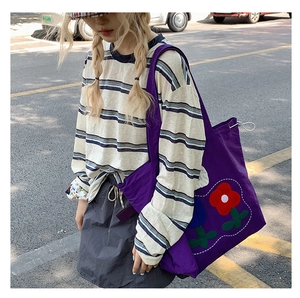 Detail of purple canvas tote bag featuring floral embroidery and wavy stitch accents
