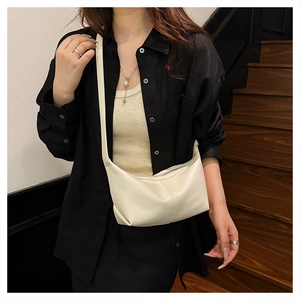 Model wearing a minimalist cream PU leather dumpling shoulder bag on an indoor staircase