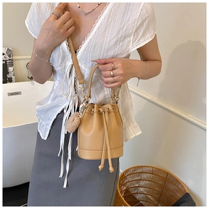 Light brown leather bucket bag with drawstring and plush charm shown in a cozy interior