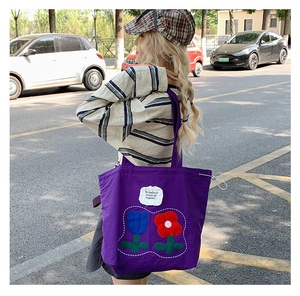 Detail of purple canvas tote bag with tulip embroidery and inspirational text label