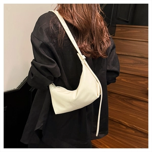Close-up of a creamy white crescent bag worn by a model against a wooden staircase