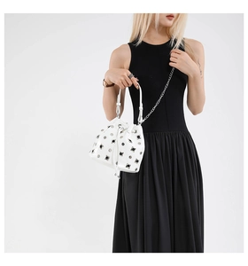 Detail of white bucket bag featuring silver rivets, drawstring closure and chain strap