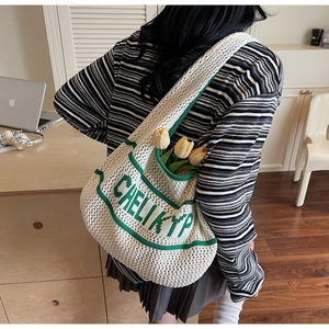 Detail of hollow knit tote bag in cream white featuring green lettering and side pocket