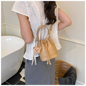 Beige pebble leather bucket bag with drawstring closure and cute plush bear charm decoration
