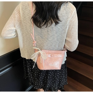Detailed view of pink crossbody bucket bag with lace bow and pearl charm on a model