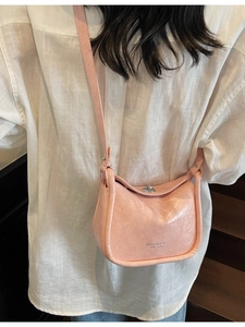 Pink wrinkled leather crossbody bag with silver buckle worn by a model on stairs