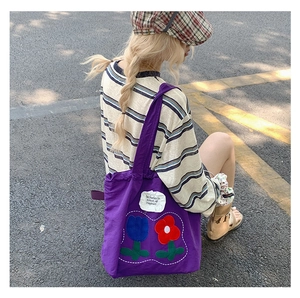 Detail of purple canvas tote bag featuring large tulip embroidery and brand patch