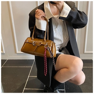 Detail view of brown glossy leather handbag featuring retro buckles and woven rope charm