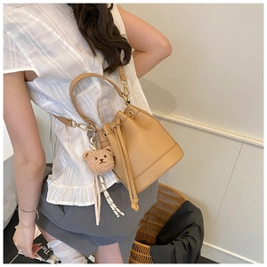 Detail of camel bucket bag with lychee pattern, drawstring closure and bear charm accessory