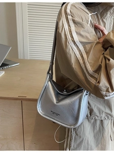 Silver metallic crossbody bag with wrinkled texture and brand lettering in a cafe setting
