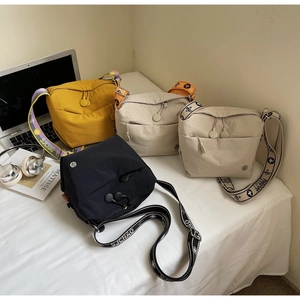 Detail view of multi-color nylon crossbody bags with wide patterned straps and zip pockets