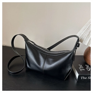 Close-up of black leather shoulder bag featuring a curved zipper and adjustable strap