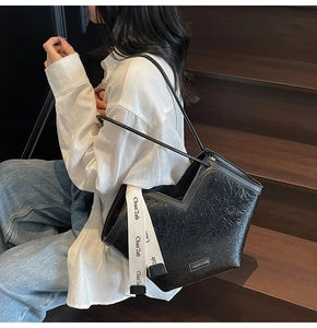 Close-up of black pleated hobo bag featuring contrast lettered strap and metallic logo