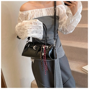 Detail of black rectangular crossbody bag with decorative strap and woven accessory